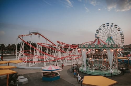 Parque de atracciones de Maspalomas con montaña rusa roja y noria verde al atardecer