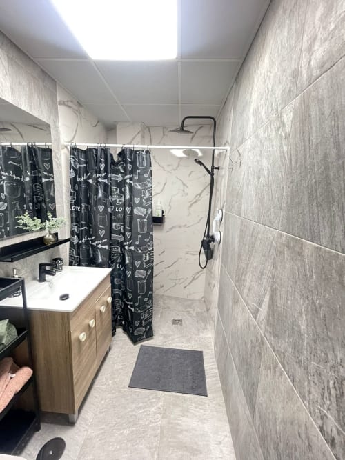 Baño moderno en Apartamentos Huelintown, Málaga con azulejos grises, ducha a ras de suelo y cortina negra con estampado