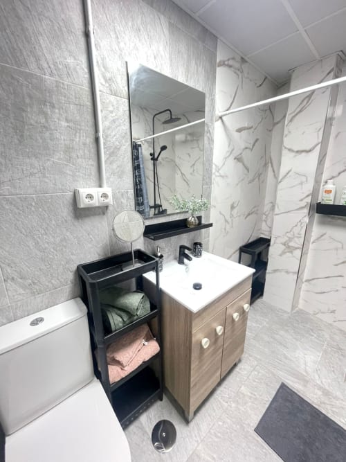 Baño moderno en Apartamentos Huelintown, Málaga con lavamanos, espejo, cabina de ducha y estantería negra de almacenamiento
