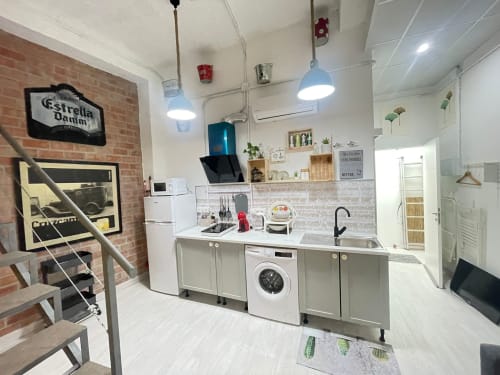 Cocina moderna en apartamento malagueño con muebles blancos, lavadora, fregadero y pared de ladrillo con letrero Stella Dartm