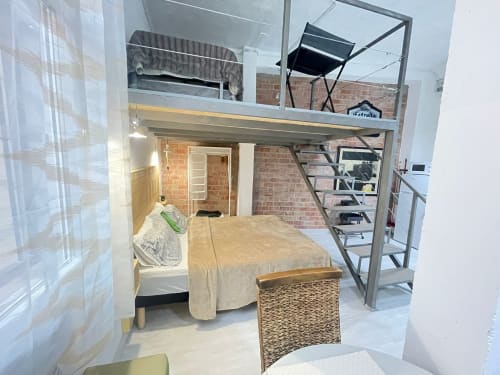 Dormitorio moderno estilo loft en Huelintown Málaga con cama en altillo, paredes de ladrillo y cocina americana