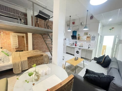 Moderno estudio en Apartamentos Huelintown, Málaga, con cocina americana, sofá gris y dormitorio en altillo