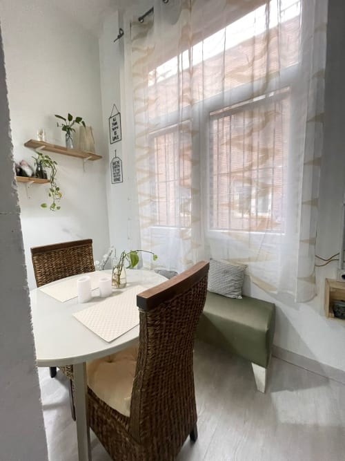 Luminoso espacio de trabajo en apartamento en Apartamentos Huelintown Málaga con escritorio, silla de mimbre, grandes ventanales, plantas en maceta y