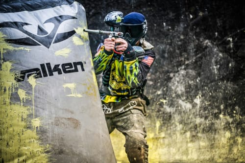 Jugador de paintball con equipo neón apuntando marcador hacia obstáculo Falken cerca de El Torno
