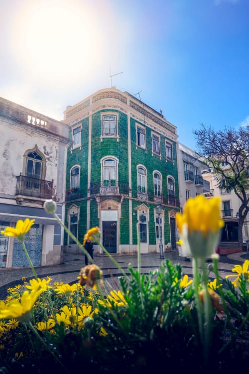 Green corner building Casa do Sol in Lagos, Algarve with yellow flowers in foreground
