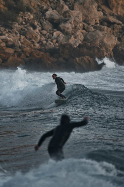 Surfer riding wave at Casa do Sol Algarve beach in Lagos, Portugal with rocky cliffs backdrop