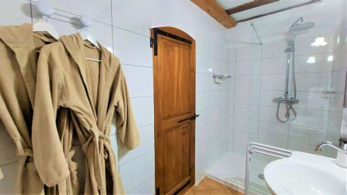 Salle de bain moderne à La Bergerie Du Moulin avec douche, lavabo blanc, porte en bois et serviettes beige
