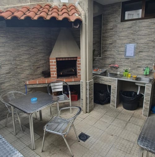 Pátio externo do hostel Sunny House em Lagos com lareira de tijolos, mesa de jantar, bancada de cozinha e área de estar