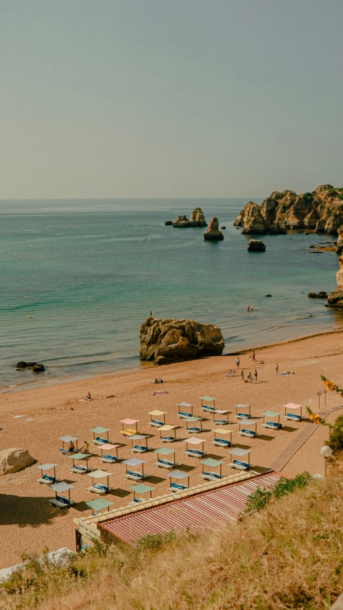 Albergue Sunny House na praia de Lagos com penhascos dourados, água turquesa e guarda-sóis