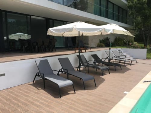 Terraço à beira da piscina da villa Casa da Luz Gerês com espreguiçadeiras, guarda-sóis e edifício moderno com vista para jardim e piscina