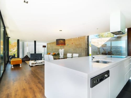 Cozinha e sala integradas modernas na villa Casa da Luz Gerês com bancadas brancas, piso de madeira e vistas para as montanhas
