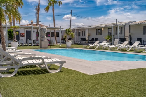 Bungalow Buda Beach resort in Chipiona with crystal blue pool, white lounge chairs, white bungalows, and palm trees under