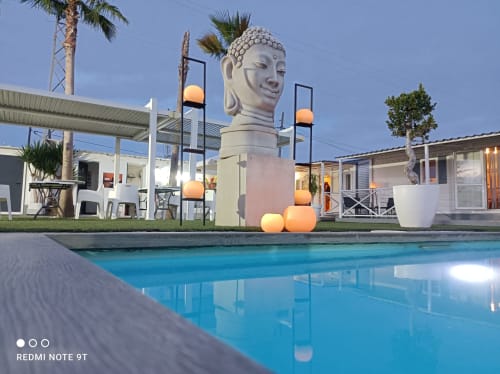 Bungalow buda beach Chipiona: poolside view with Buddha statue, lounge chairs, palm trees, and modern white bungalows at dusk