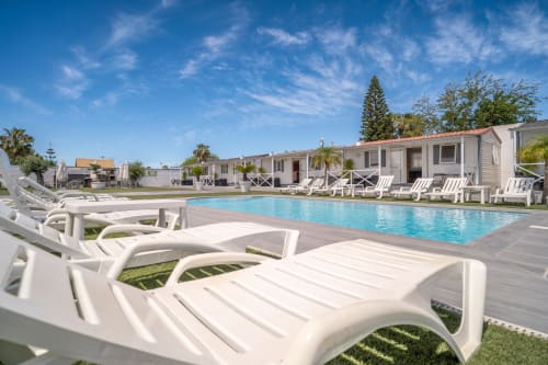 Bungalow Buda Beach pool area in Chipiona with white loungers, crystal blue water, and beachside bungalows under sunny skies