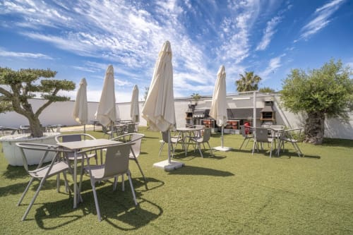 Outdoor garden terrace at Bungalow Buda Beach in Chipiona with dining tables, cream umbrellas, and Mediterranean landscape