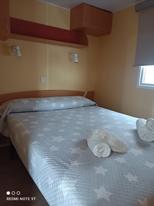 Bedroom at Bungalow Buda Beach in Chipiona with queen bed, rolled towels, yellow walls, and red wooden furnishings