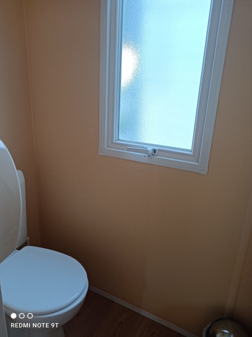 Bathroom in Bungalow B at Buda Beach hotel, Chipiona, with white toilet and frosted window with garden view