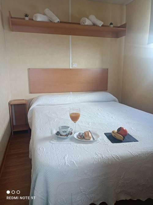 Cozy bedroom at Bungalow Buda Beach hotel in Chipiona with white bed, wooden headboard, shelf with rolled towels, breakfast