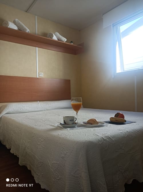 Bright bedroom in Bungalow E at Buda Beach hotel in Chipiona with white bed, breakfast tray, and garden view window.