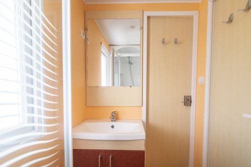 Modern bathroom in Bungalow F at Buda Beach hotel, Chipiona, with white sink, mirror, and orange-tiled walls