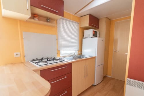 Modern kitchen in Bungalow F at Buda Beach hotel, Chipiona with gas stove, sink, refrigerator and yellow walls