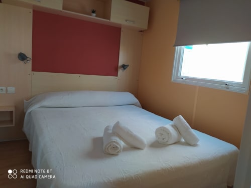 Bright bedroom at Bungalow Buda Beach with double bed, white linens, rolled towels, red headboard, and garden view window in