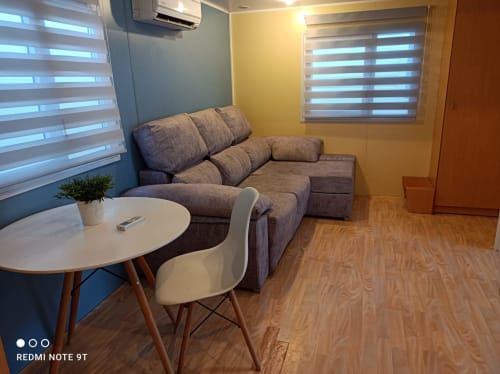 Modern living area in Bungalow I at Buda Beach hotel with gray sofa, round dining table, and striped blinds in Chipiona