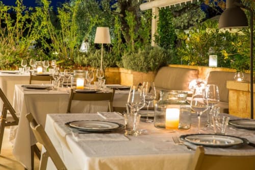 Elegante cena all'aperto a Masseria Picca Picca con tavoli illuminati da candele, calici di vino e rigogliosa vegetazione a Morciano di