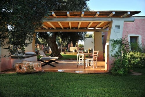 Pergolato in legno sul patio della Masseria Picca Picca B&B a Morciano di Leuca, con sedie da pranzo e ulivo.