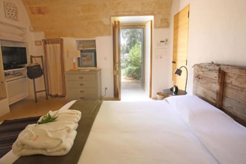 Camera luminosa con letto bianco, testata rustica, angolo cottura e vista sul giardino della Masseria Picca Picca a Morciano di Leuca