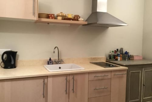 Modern kitchen in Lourmarin courtyard apartment with light wood cabinets, white sink, stainless steel range hood, and cream