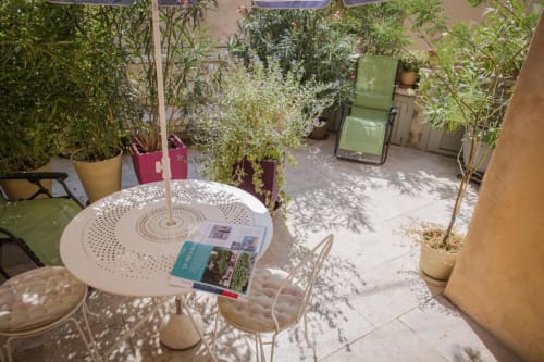 Shaded patio garden at Ancienne Maison des Gardes in Lourmarin with white table, chairs, and potted plants creating a