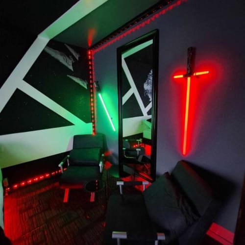 Chambre illuminée aux néons modernes à l'hôtel Les Deux Porches à Verrières, avec croix rouge et motifs géométriques verts