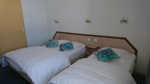 Lits jumeaux avec draps blancs et oreillers bleu-vert à l'hôtel Les Deux Porches à Verrières