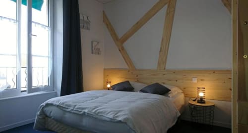 Chambre moderne aux Deux Porches à Verrières avec lit en bois, literie blanche, coussins noirs et éclairage ambiant