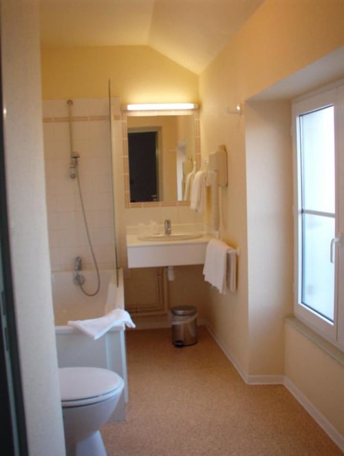 Salle de bain moderne de l'hôtel Les Deux Porches à Verrières avec douche vitrée, lavabo, toilettes et radiateur-sèche-serviettes