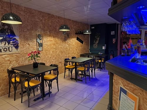 Espace bar et restaurant contemporain de l'hôtel Les Deux Porches à Verrières avec tables noires, chaises jaunes et ambiance bleue