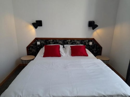 Chambre moderne de l'hôtel Les Deux Porches à Verrières avec literie blanche, oreillers rouges et tête de lit noire avec appliques murales