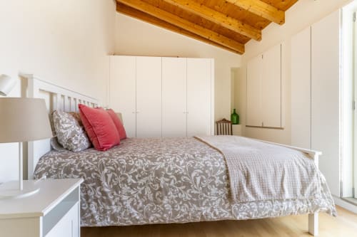 Quarto luminoso na villa Casa Hortas, Bordeira com cama branca, roupa de cama estampada, almofadas rosa e vigas de madeira aparente