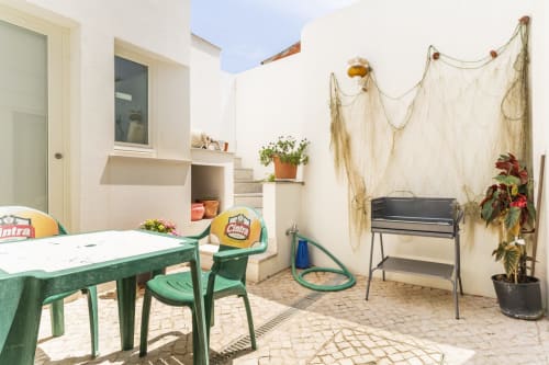 Pátio externo da villa Casa Hortas em Bordeira com mesa de jantar verde, churrascaria e plantas em vasos
