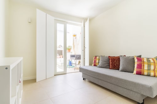 Sala luminosa com sofá cinzento, almofadas coloridas e portas de vidro que abrem para varanda na villa Casa Hortas em Bordeira,
