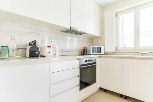 Cozinha moderna branca com painel de mármore, forno elétrico, eletrodomésticos e janela na villa Casa Hortas, Bordeira Portugal