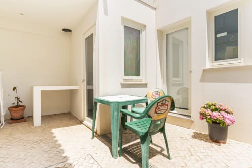 Pátio coberto da villa Casa Hortas em Bordeira com móveis vintage verdes, flores rosa e vista para as montanhas