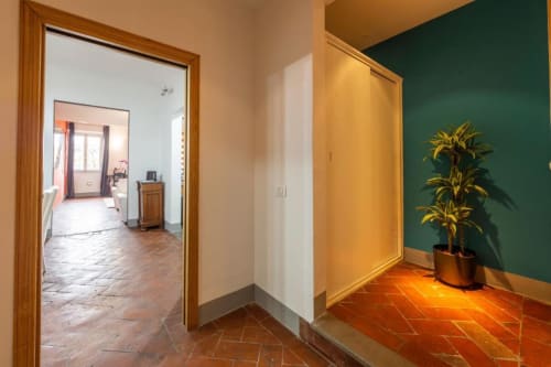 Luminoso corridoio con pavimenti in cotto, parete verde, pianta in vaso e porte in legno dell'Appartamento Fiorentino