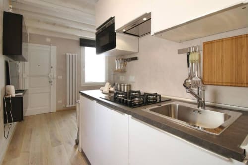 Cucina moderna nel mio Appartamento Fiorentino con mobili bianchi, fornello a gas, lavello in acciaio inox e piano di lavoro grigio