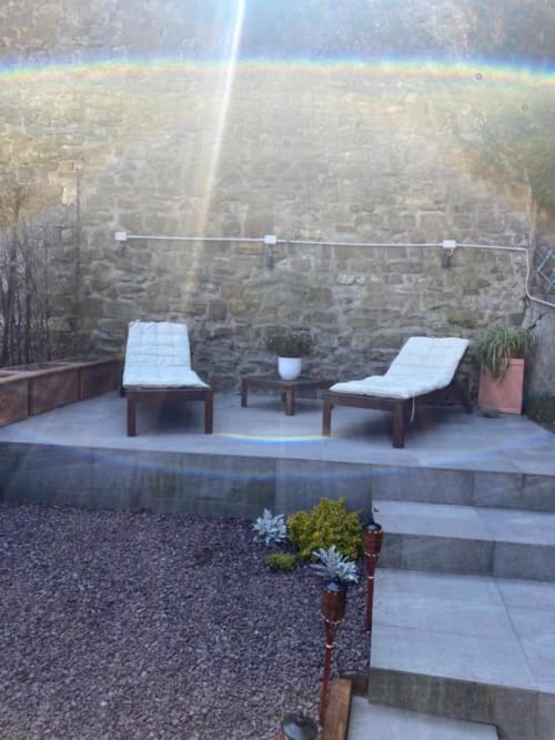 Giardino di appartamento fiorentino con due sedie a sdraio, muro in pietra e piante in vaso al sole
