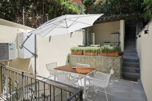 Terrazza giardino di appartamento fiorentino con ombrellone a sbalzo, tavolo da pranzo in legno, sedie bianche e vasi di piante
