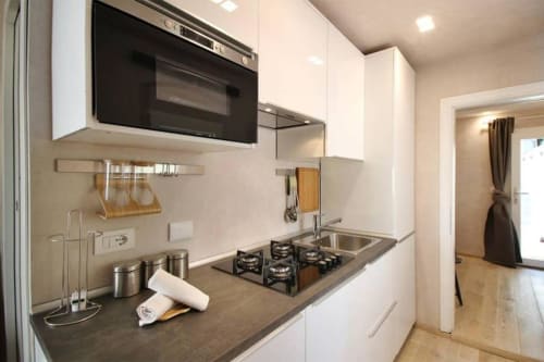 Cucina moderna dell'appartamento fiorentino con cabinetry bianco, piano cottura a gas, microonde e piano di lavoro scuro