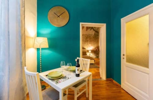 Elegante zona pranzo di My Florentine Apartment con pareti turchesi, tavolo in legno apparecchiato per due, accesso alla camera da letto