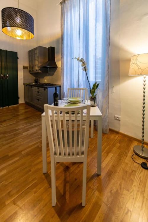 Zona pranzo di moderno appartamento fiorentino con sedia bianca, tavolo rotondo, cucina, lampada a sospensione e orchidea accanto alla finestra